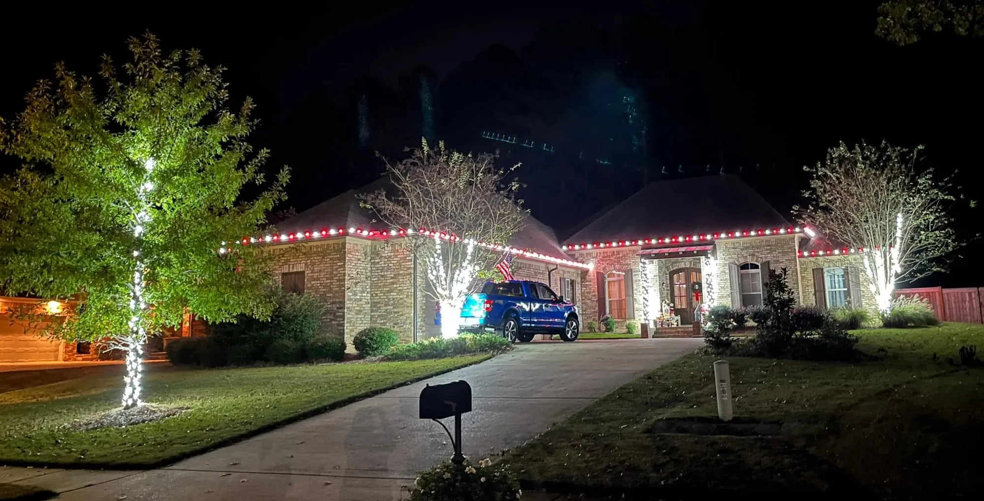Front yard at night with a lit tree and red and white lights along the rooflines
