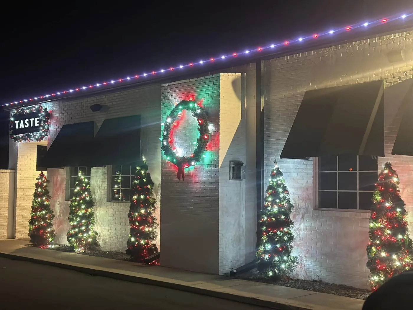 Storefront with lit rooflines, wreath and decorated trees at night